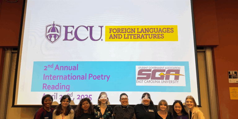 Nine students stand smiling in front of a large projected screen displaying the event title, “2nd Annual International Poetry Reading,” along with ECU’s Foreign Languages and Literatures and Student Government Association logos.